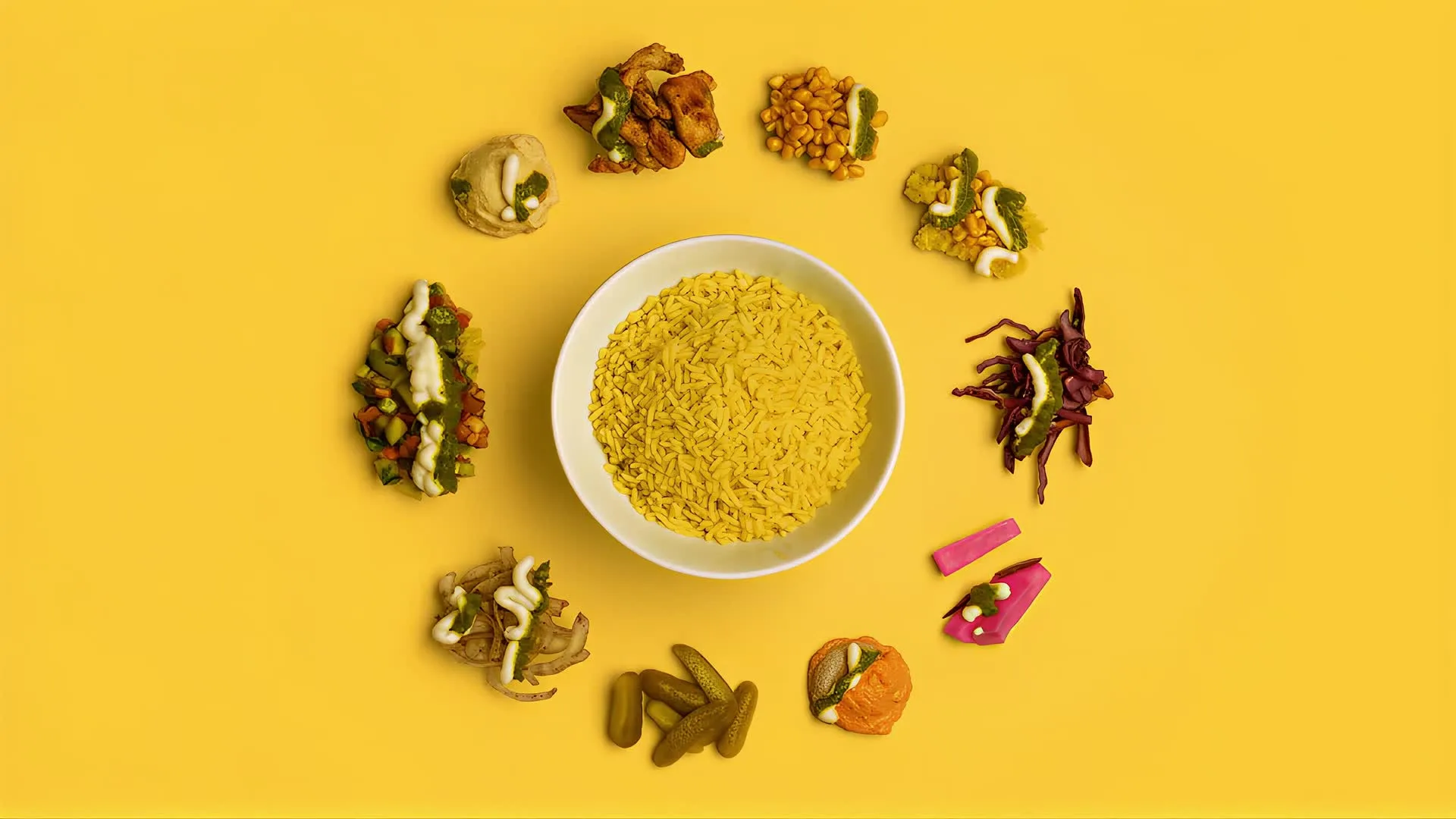 A bowl of saffron rice on Amba yellow, ringed by every topping that went into it