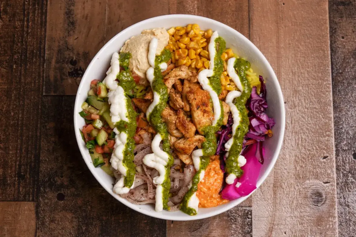 Chicken shawarma bowl with hummus, corn, cabbage and toum and zhug drizzles